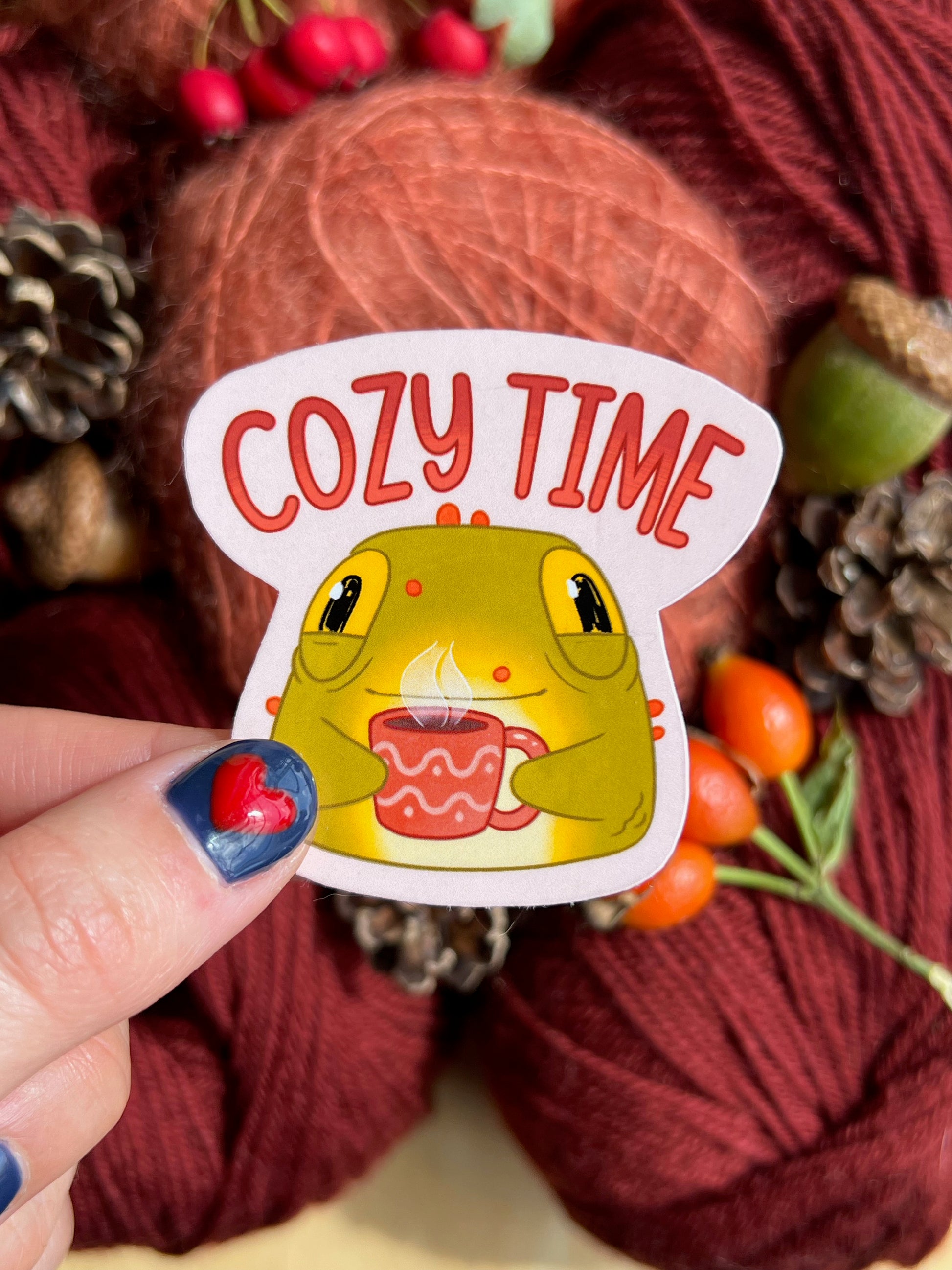 Toad sticker holding a mug on a cozy autumn themed background. The text on the product reads Cozy Time.