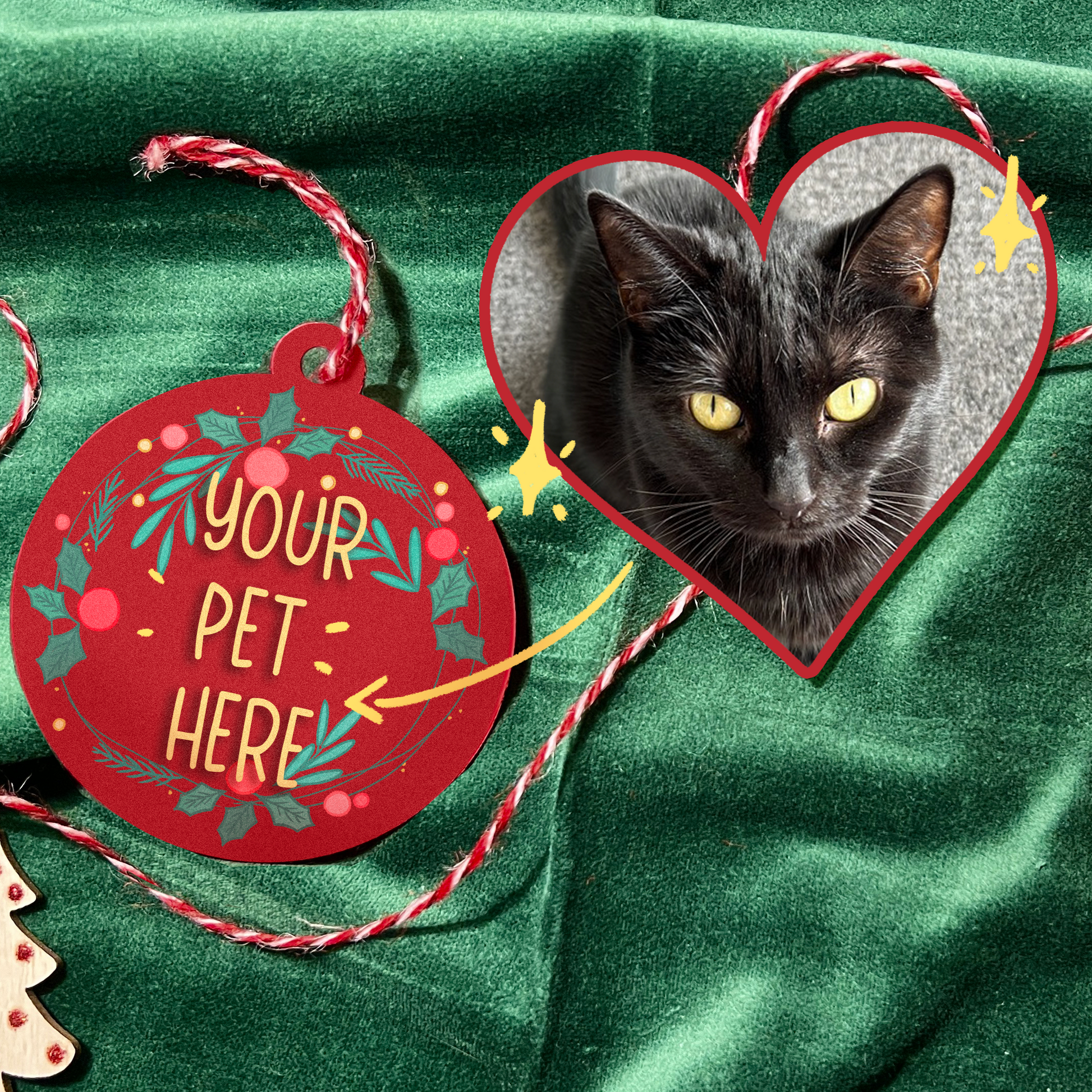 A festive display showcasing a custom pet-themed Christmas bauble on a lush green velvet background. The left bauble features the text "Your Pet Here," surrounded by a vibrant wreath of holly and berries on a red background.  In the center, a heart-shaped cutout highlights a sleek black cat with bright yellow eyes, framed by playful sparkles. The scene is decorated with red-and-white twine, miniature pinecones, and wooden Chris