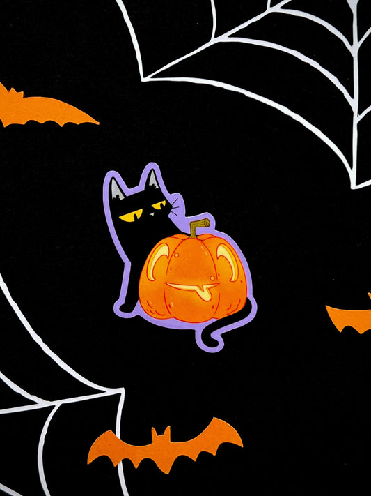 Black cat sticker behind a pumkin with a purple background.