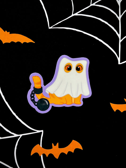 Die cut sticker of an orange cat dressed as a ghost, with a chain around its tail, on a black backdrop.