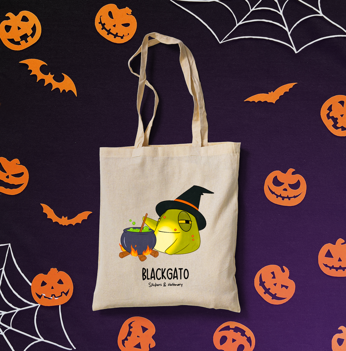 Cotton tote bag, featuring a toad dressed as a witch with a cauldron, on a dark Halloween backdrop.